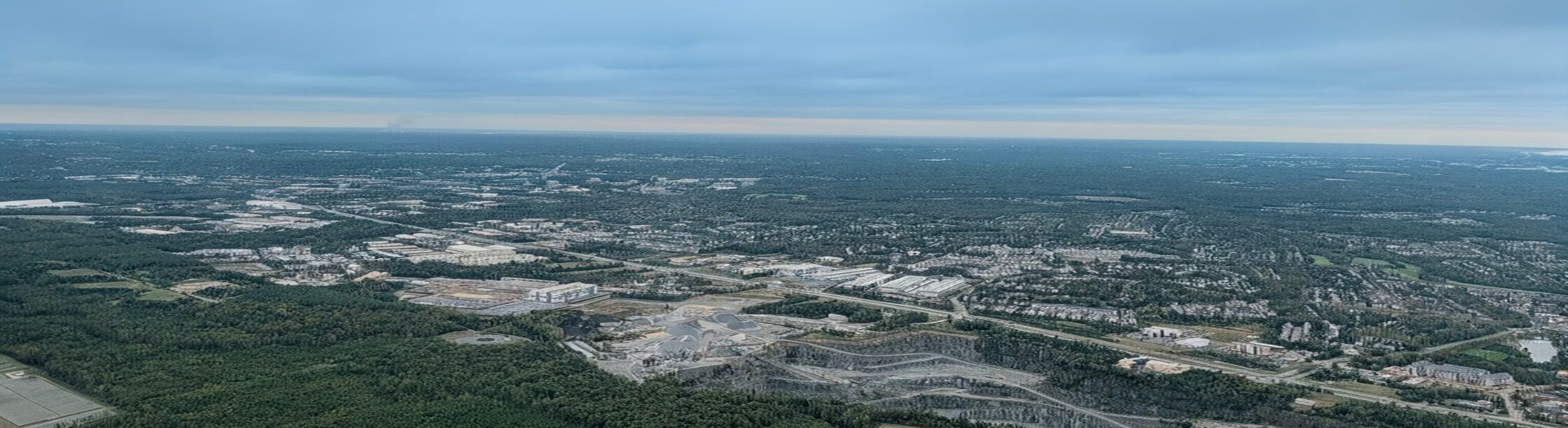 Aerial view of Northern Virginia showcasing commercial and industrial development surrounded by green landscapes under a cloudy sky.