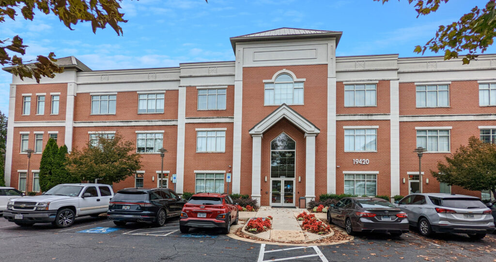 Exterior view of 19420 Golf Vista Plaza, a red brick medical office building in Leesburg, VA, with a parking lot in front, recently sold by Serafin Real Estate.